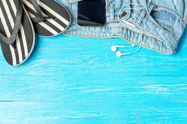 Frame elegant female slippers jeans smartphone earphones on blue wooden background, copyspace for text, summer vacation. - Foto, Imagem