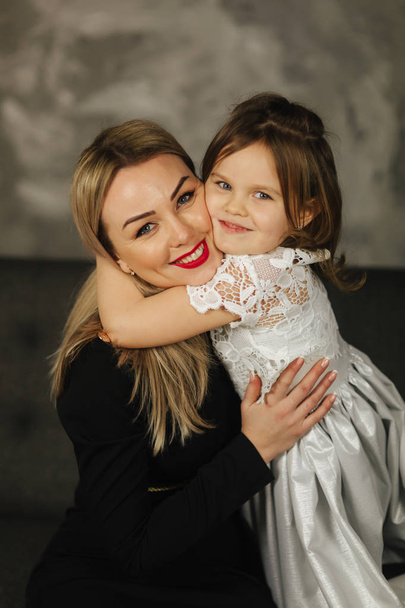 Little girl hug mother and smile. Happy young mom with her daughter at home - Foto, Bild