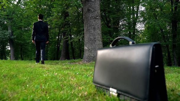 Homme laissant la mallette sur l'herbe et marchant dans la forêt, échapper mode de vie occupé
 - Photo, image