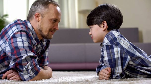 Boy and father lying on floor and looking at each other, making contact with kid - Foto, imagen