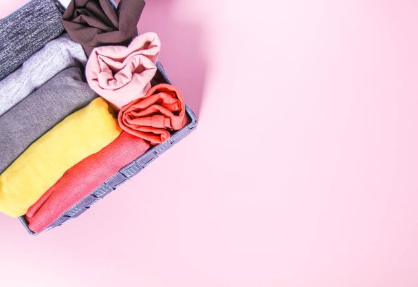 bunte Kleidung vertikale Lagerung im heimischen Kleiderschrank. Kleidungsstücke in Textilbox auf zartem rosa Hintergrund - Foto, Bild