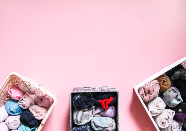 bunte Kleidung vertikale Lagerung im heimischen Kleiderschrank. Kleidungsstücke in Kunststoff- und Textilboxen auf sanftem rosa Hintergrund. - Foto, Bild