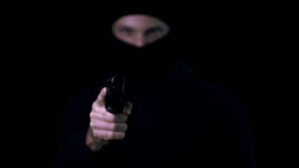Silhouette of criminal in balaclava aiming gun armed robbery, black background - Фото, зображення