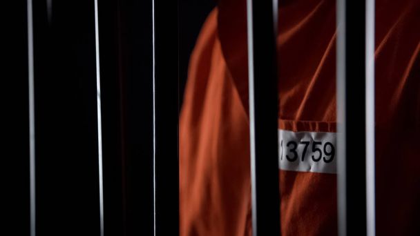 Prisoner in orange uniform standing behind bars, punishment for committed crime - Fotoğraf, Görsel