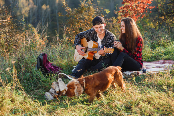 Young man playing on the guitar for his lovely girlfriend. Happy couple with guitar resting on picnic in spring park. - 写真・画像