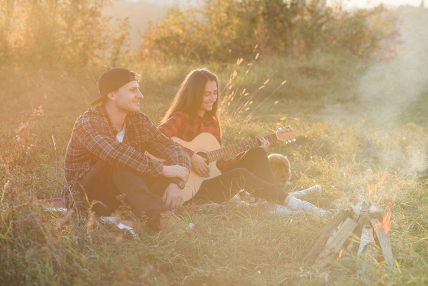 Young man playing on the guitar for his lovely girlfriend. Happy couple with guitar resting on picnic in spring park. - Fotoğraf, Görsel