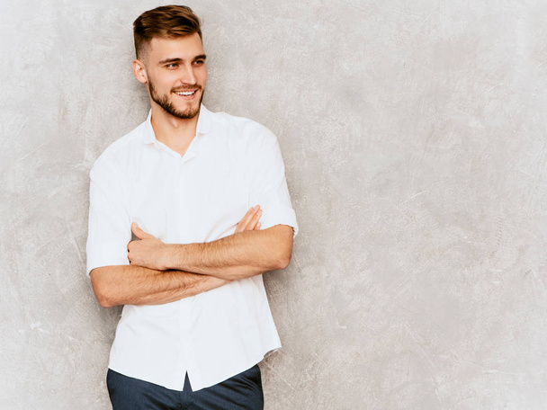 Портрет гарного усміхненого хіпстера-бізнесмена моделі в повсякденній літній білій сорочці. Модний стильний чоловік позує на сіру стіну. Перехрещені руки
 - Фото, зображення
