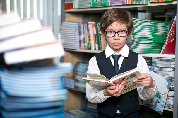 A boy in school uniform in the library is standing with a book.  - Foto, Imagen