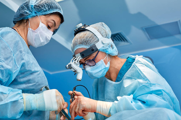 Portrét profesionálních lékařů během operace na modrém pozadí. Koncept chirurgie, lékařství. Chirurgové pracují na složitá operace - Fotografie, Obrázek