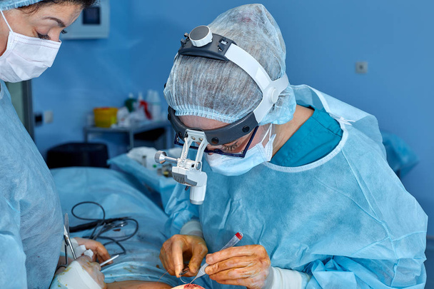 Sebész portréja varr fel a beteg műtét után. Koncepció a műtét. Kék háttérrel műtét során a sebész - Fotó, kép