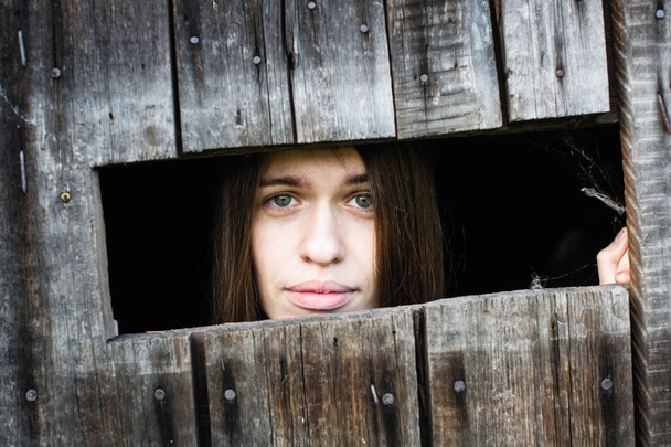 Γυναίκα με μακριά μαλλιά και όμορφα χείλη, κοιτάζει έξω από τα παράθυρα ξύλινο υπόστεγο. - Φωτογραφία, εικόνα