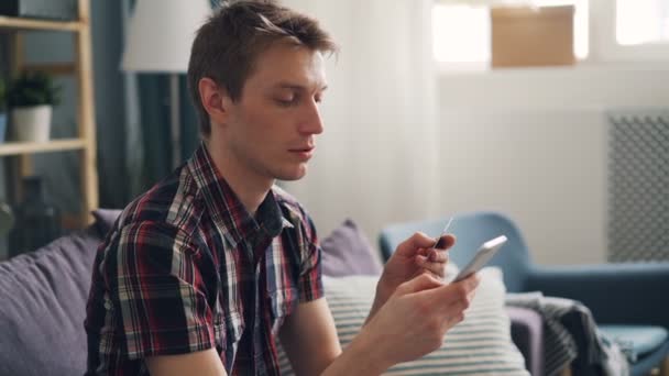 Good-looking man is making electronic payment with credit card and smartphone touching screen then smiling enjoying modern technology. Millennials and banking concept. - Materiał filmowy, wideo
