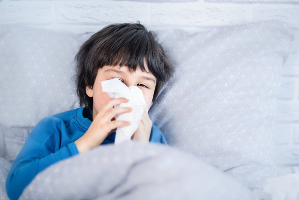Sick little child boy with cold rhinitis blowing his nose with napkin in bed, concept of flu season  - Valokuva, kuva