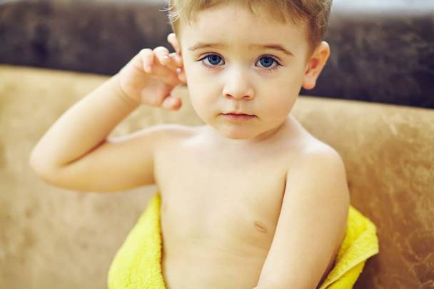 boy wrapped in a towel drying after shower while sitting on couch - Фото, изображение