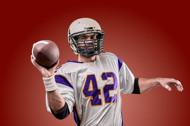 American football player in uniform with the ball is preparing to make a pass. American football concept, brown background - Photo, Image