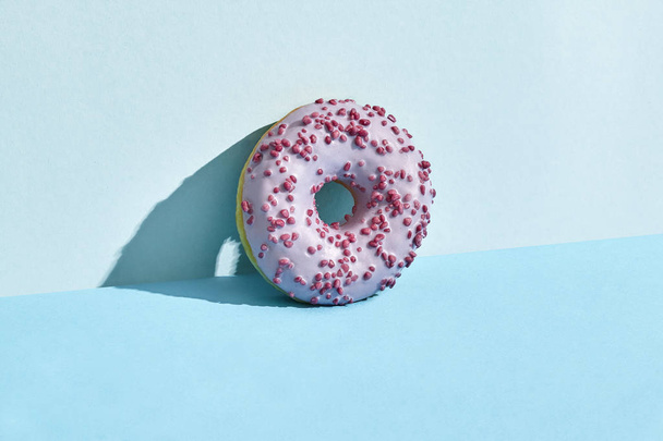 Food design. Close up high quality image of pink glazed donut on blue background - Foto, Imagen