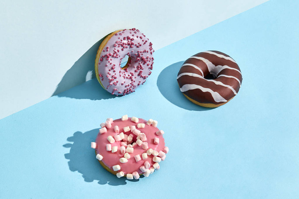 Três doces saborosos donuts em caramelo e cobertura de chocolate, em um fundo de duas cores
 - Foto, Imagem