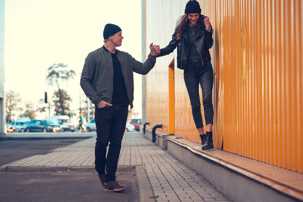 Young couple in love walks by the sity. Spring, autumn. The guy is wearing a jacket and hat. Girl in a hat and leather jacket with a scarf - Фото, изображение