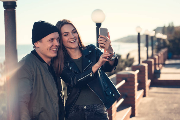 Mladý milující pár stráví zábavu čas od moře a dělá selfie. Muž a žena mají jarní oblečení - Fotografie, Obrázek
