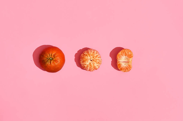 Diseño de alimentos. Composición de mandarina entera, mandarina pelada y la mitad de mandarina pelada sobre fondo de coral rosa
 - Foto, imagen