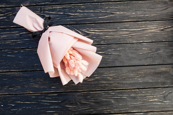 Hermoso ramo de flores rosas secas sobre un fondo negro de madera. Minimalismo, espacio para el texto. Tarjeta de regalo
 - Foto, Imagen