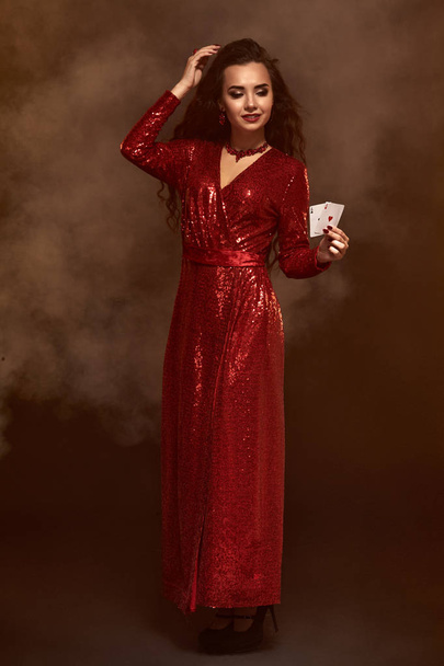 Giovane bella bruna fortunata in un abito da sera rosso mostra le sue carte, un paio di assi
 - Foto, immagini