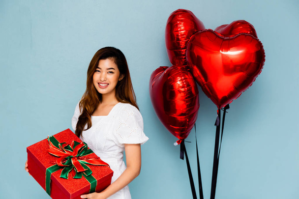 Glimlachende Aziatische vrouw met gift in de buurt van ballonnen - Foto, afbeelding