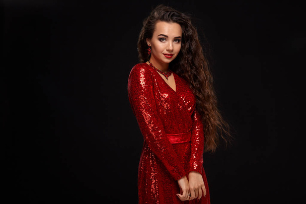 Charming young caucasian brunette woman in red cocktail dress posing before camera on black background in studio - Fotografie, Obrázek