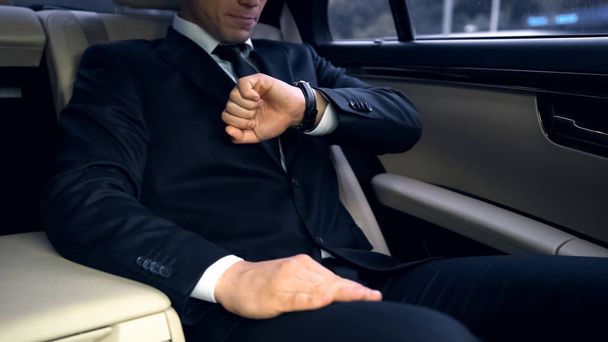 Бізнесмен їде на задньому сидінні в розкішному автомобілі, дивлячись на годинник, пізно на зустріч
 - Фото, зображення