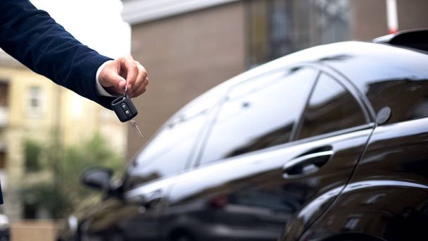 Salesman giving car key to buyer, dealership showroom, auto rental, luxury - Fotó, kép