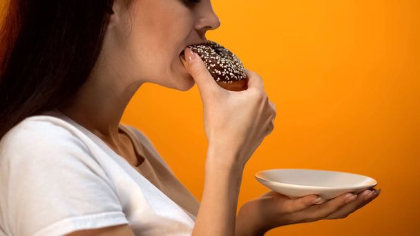 Girl biting chocolate donut, high-calorie sweet food, increased glucose diabetes - Foto, imagen