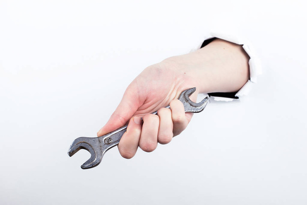Female hand out of a hole in paper, holds a wrench. Isolate on white background to labor day. - Fotografie, Obrázek