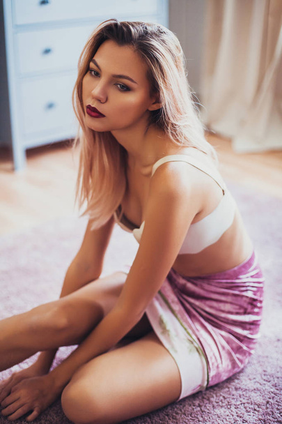 Beautiful young woman in bedroom, wearing bra and velvet skirt. - Photo, Image