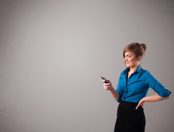 young lady standing and holding a phone with copy space - Фото, изображение