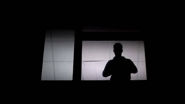 Silhueta de paciente homem em lunático na janela de asilo, deficiências psicossociais
 - Foto, Imagem