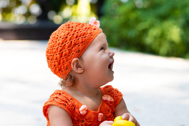 uma menina em um vestido de malha laranja e chapéu é surpreendida, se alegra, grita, chora, levanta as mãos. conceito de moda infantil
. - Foto, Imagem