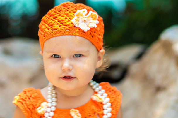 tyttö oranssi neulotut mekko ja hattu on yllättynyt, iloitsee, huutaa, itkee, nostaa kätensä. lasten muoti käsite
. - Valokuva, kuva