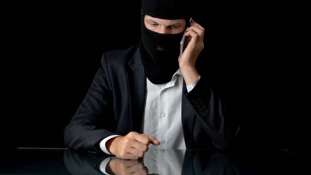 Assassino mascarado falando em smartphone com parceiro de crime, assassinato por contrato, arma
 - Foto, Imagem