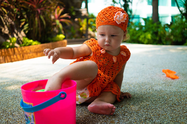 a lány egy narancssárga kötött ruha és kalap meglepett, örül, sikolyok, sír, emeli a kezét. gyermek divat fogalma. - Fotó, kép