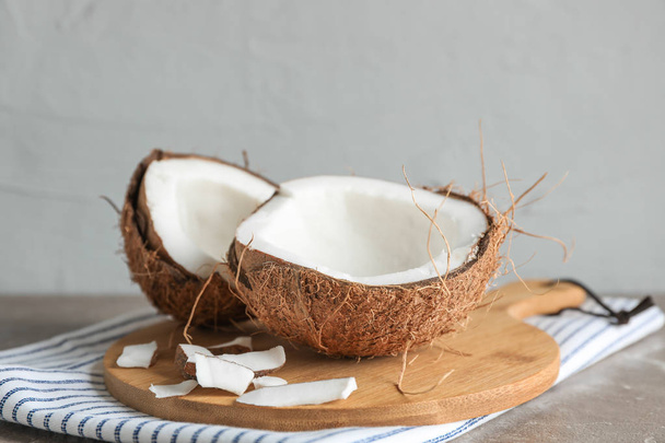 Cutting board with split coconut on table against grey backgroun - Φωτογραφία, εικόνα