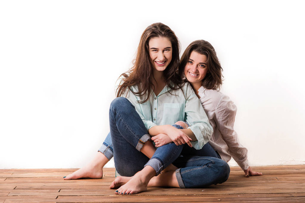 Attractive girls sit at wooden floor in hugs - Фото, зображення