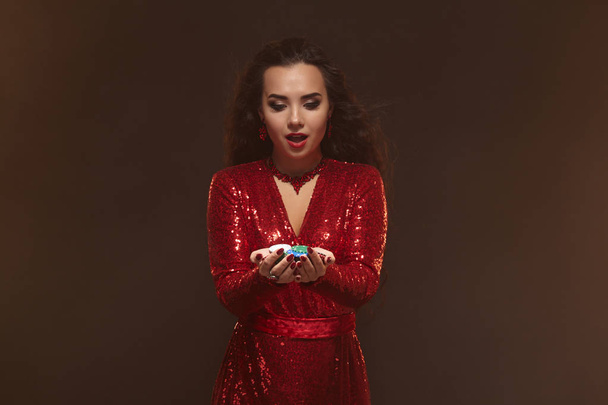 Giovane donna bruna piuttosto fortunata in un abito da sera rosso tiene chip di poker nelle sue mani, mostrando le sue vincite
. - Foto, immagini