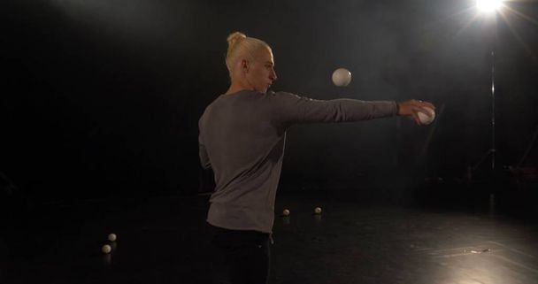 Жонглер в черной студии делает трюки с мячами
. - Фото, изображение