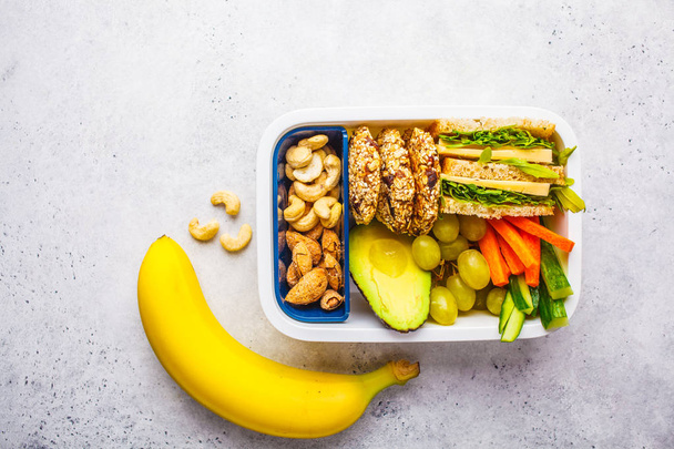 School healthy lunch box with sandwich, cookies, fruits and avoc - Фото, изображение