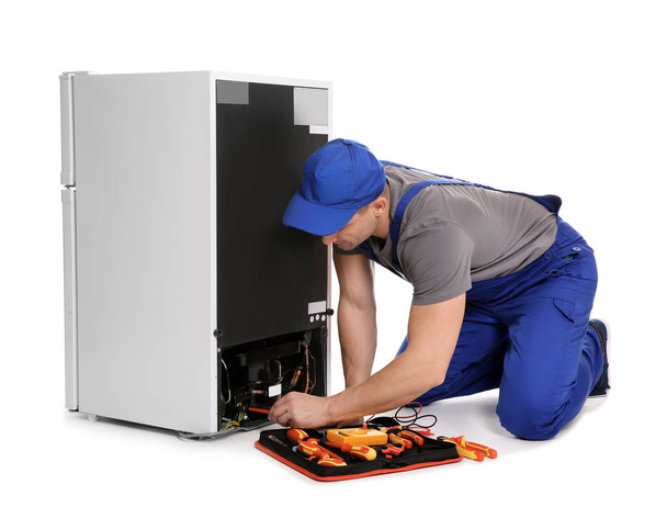 Male technician in uniform repairing refrigerator on white background - Фото, зображення
