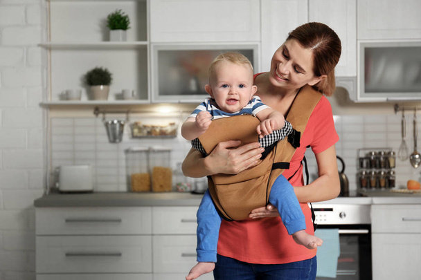 Woman with her son in baby carrier at home. Space for text - Фото, зображення