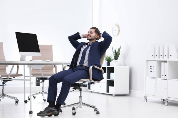 Young businessman sitting on office chair at workplace - Fotó, kép