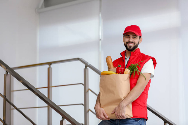 Man holding paper bag with fresh products on staircase, space for text. Food delivery service - Zdjęcie, obraz