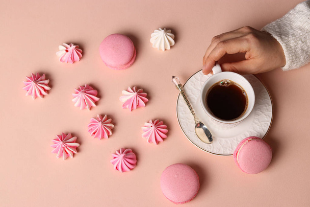 Meringue cookies and macaroons on a pink background, cup of coffee and women's hands - Фото, изображение