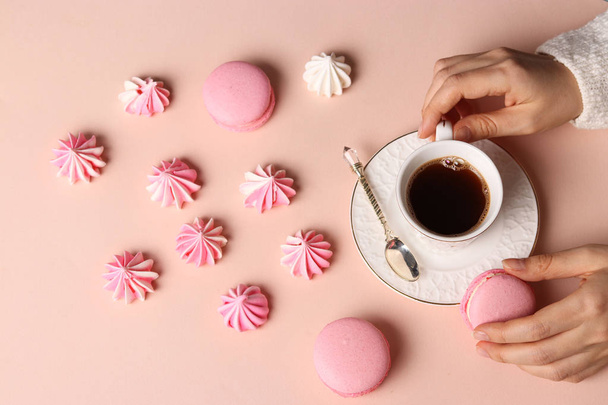 Meringue cookies and macaroons on a pink background, cup of coffee and women's hands - Φωτογραφία, εικόνα